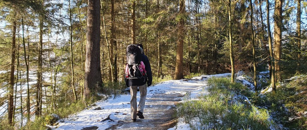 Mann mit Baby in Kraxe im Wald auf dem Liebesbankweg