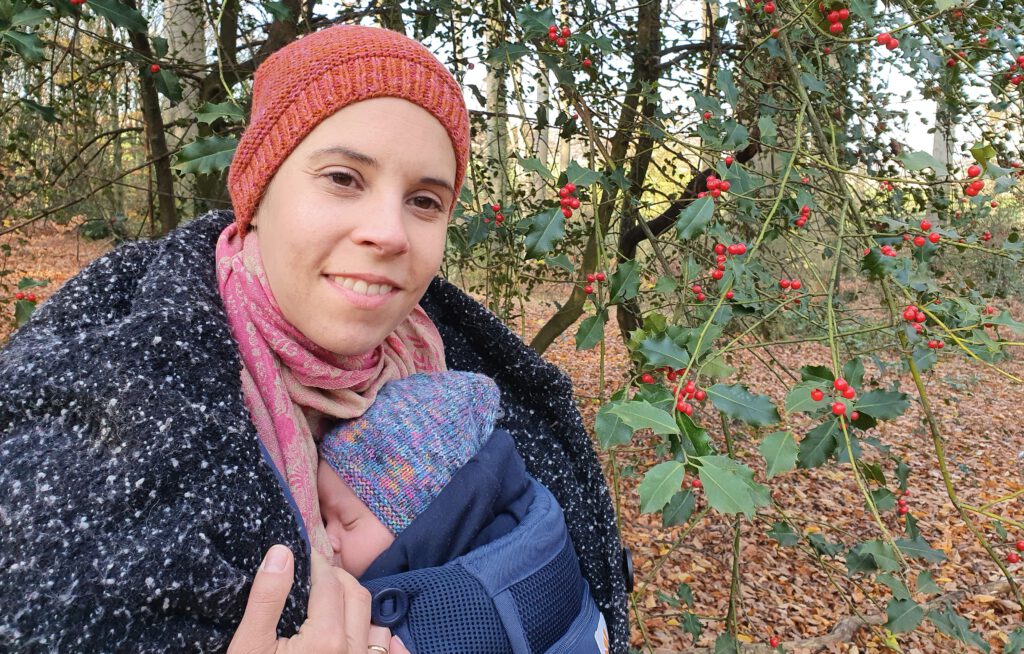 Frau mit orangener Mütze mit Neugeborenem Baby in Trage vor der Brust