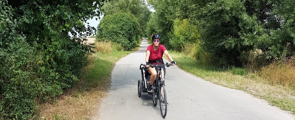 Frau auf Fahrrad mit Radanhänger auf Weg zwischen Hecken und Bäumen